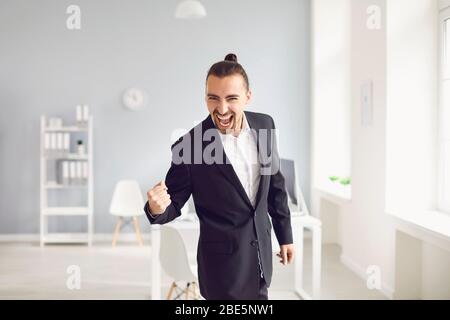 Businessman in a black suit shouts celebrates a successful contract standing in a modern office. Stock Photo