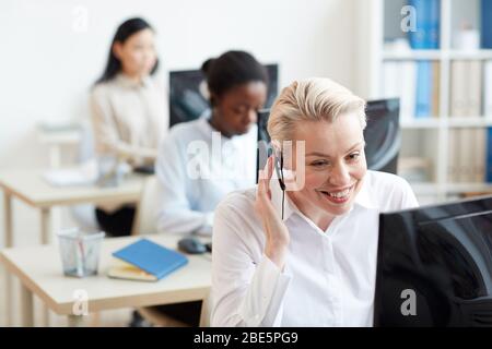 Portrait of female hotline operators sitting at desks in row , focus on smiling woman talking to customer via headset, copy space Stock Photo