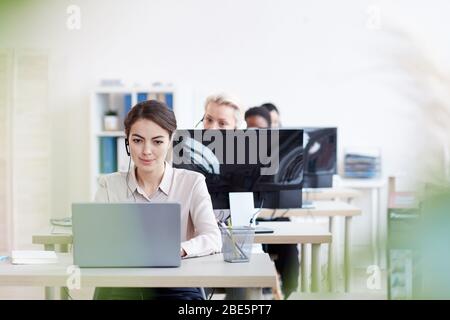 Portrait of female helpdesk operators sitting at in row , focus on elegant young woman talking to customer via headset, copy space Stock Photo
