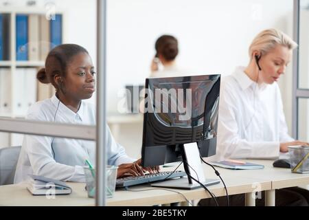 Multi-ethnic group of female call center operators using computers at workplace, focus on young African-American woman wearing headset in foreground, Stock Photo