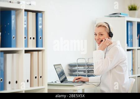 Portrait of modern businesswoman wearing headset and smiling at camera while working from home, copy space Stock Photo