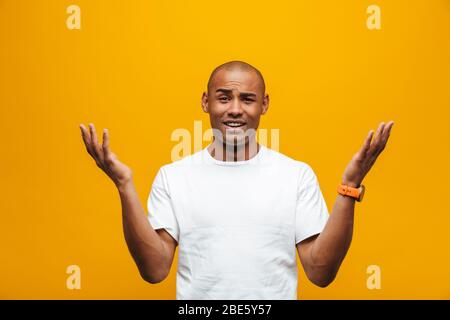Portrait of an attractive confused casual young african man standing over yellow background, gesturing Stock Photo