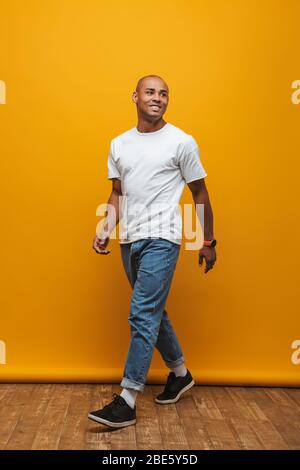 Full length portrait of an attractive happy confident casual young man walking over yellow background Stock Photo