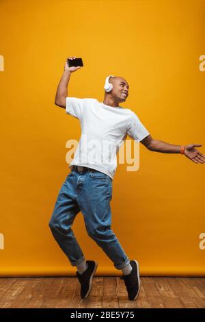 Full length portrait of an attractive happy confident casual young man jumping over yellow background, dancing Stock Photo