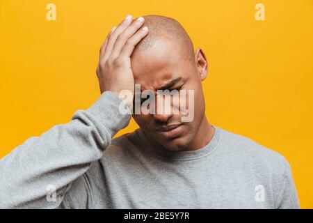 Portrait of an attractive upset casual young african man standing over yellow background, suffering from a migraine Stock Photo