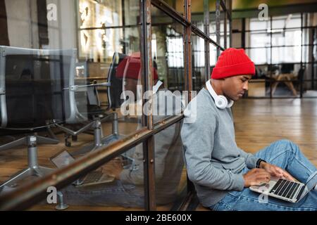 Image of young attractive african american man wearing hat using laptop computer while working in office Stock Photo