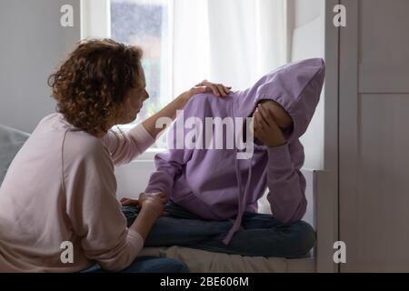 Caring mother comforting sad crying teenage daughter sitting on bed Stock Photo