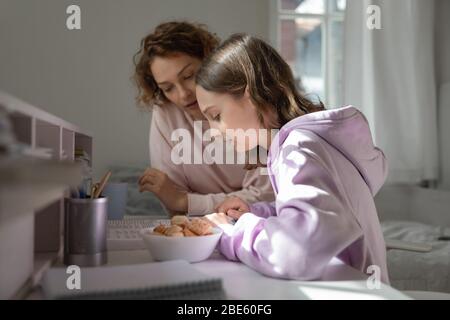 Focused mom helping teenage daughter doing homework studying from home Stock Photo