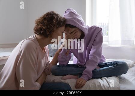 Worried mom comforting depressed teen daughter crying at home Stock Photo
