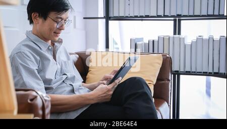 Senior Asian man playing tablet and video call on sofa in living room at home  Portrait of Asian elderly man is Relaxing and Happiness With playing ta Stock Photo