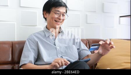 Senior Asian man using smart phone shopping online and paying with credit card at home Stock Photo