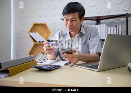 Senior Asian man using smart phone shopping online and paying with credit card at home Stock Photo