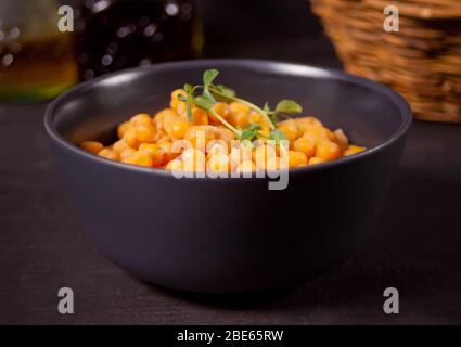 Cooked chickpeas with fresh herbs in black bowl. Healthy and vegetarian food. Stock Photo