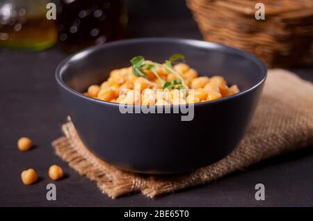Cooked chickpeas with fresh herbs in black bowl. Healthy and vegetarian food. Stock Photo