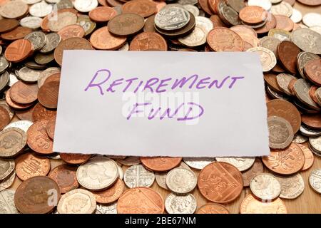 The words retirement fund written in purple pen on white paper, the paper is on top of hundreds of silver and copper coloured British coins Stock Photo