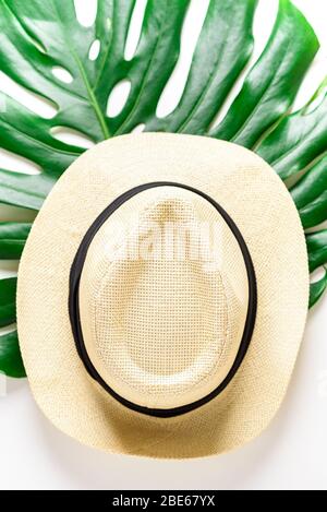 Traveler accessories. Straw hat and tropical palm monstera leaf on white background. Travel vacation concept. Summer background. Flat lay, top view. Stock Photo