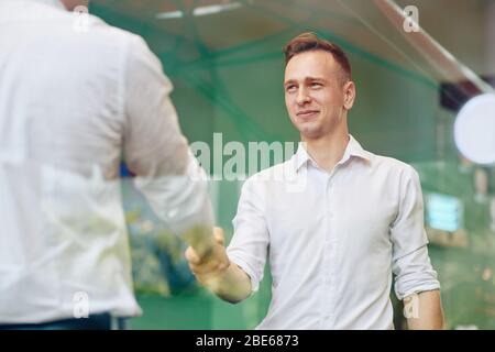 Smiling handsome young entrepreneur shaking hand of colleague before meeting Stock Photo