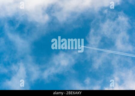 Unidentified distant airplane and vapour trail in blue sky dotted with fluffy white clouds. Metaphor foreign travel, aviation industry, holidays. Stock Photo