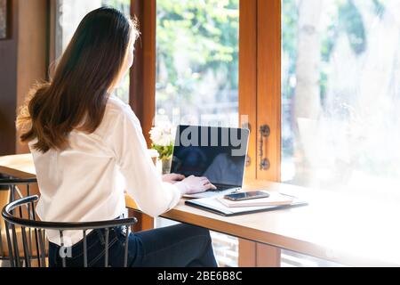 Quarantine Young asian woman wearing smart casual clothes work at home in living room using laptop and drinking hot coffee and croissant while city  l Stock Photo
