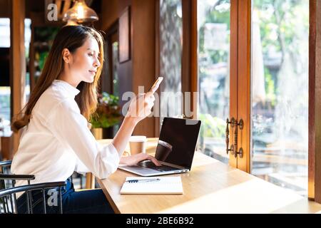 Quarantine Young asian woman wearing smart casual clothes work at home in living room using laptop and drinking hot coffee and croissant while city  l Stock Photo