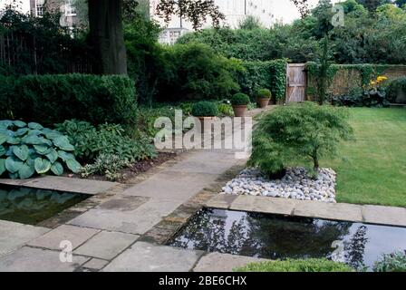 York stone path over a canal to a garden gate with hostas, japanese maple  and box balls in pots. Stock Photo