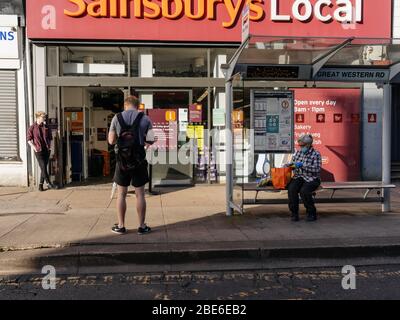 Woman sitting in a bus stop wearing a surgical mask outside a Sainsbury's Local supermarket in Glasgow during the UK Coronavirus pandemic lockdown. Stock Photo