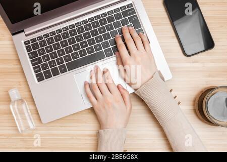 Hand sanitizer near the womans hands on a keyboard. Coronavirus prevention using antibacterial alcohol gel on a work place. Stock Photo