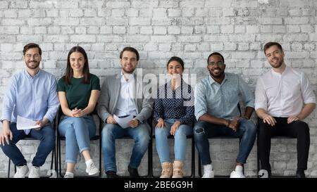 Portrait of happy multiracial candidates sit in row in hallway Stock Photo