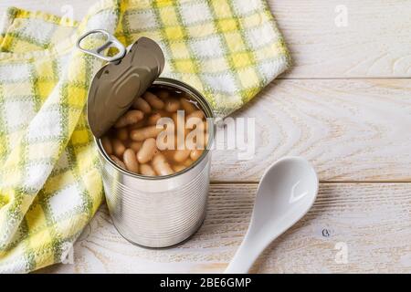 Canned backed beans in an open tin can with pull tab near ceramic spoon on a wood table. Vegetable protein and ingredient for vegetaran food. Stock Photo