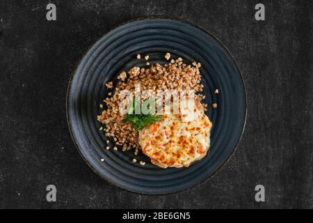 Top view of chopped pork meat baked with cheese and tomato served with buckwheat porridge Stock Photo