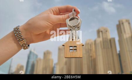 Real estate purchase concept. The girl holds the keys to a new house on the background of a Dubai skyscraper. Stock Photo