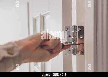Man remove the door. Twists self-tapping screw with a screwdriver. Stainless door hinges on a white door. Stock Photo