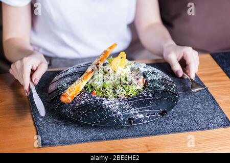 Woman is eating healthy lunch on dark background. Salad with parmesan cheese Stock Photo