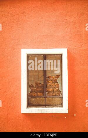 Broken glass in window on orange color plaster cement wall with white frame casing window. Broken or Cracked Window. Stock Photo