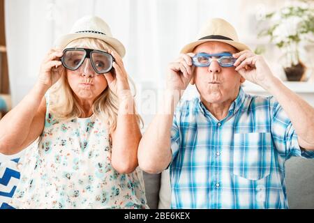 Senior couple sitting in travel agency sitting wearing hats and swimming glasses funny grimace Stock Photo