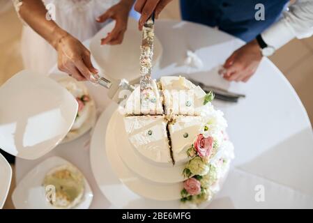 bride and a groom is cutting their stylish wedding cake on wedding banquet. Newlyweds holding knife and cutting together wedding cake Stock Photo