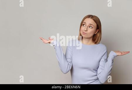 I don't know! Close up studio portrait of shy awkward young woman feeling embarrassed, confused and puzzled, shrugs shoulders, does not know what happ Stock Photo