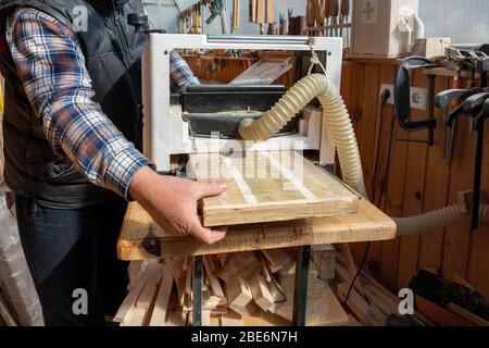 Senior craftsman woodworking at carpentry with lots of modern professional power tools. Man using thicknessing planer machine, clamp joiner, circular Stock Photo