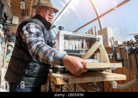 Senior craftsman woodworking at carpentry with lots of modern professional power tools. Man using thicknessing planer machine, clamp joiner, circular Stock Photo