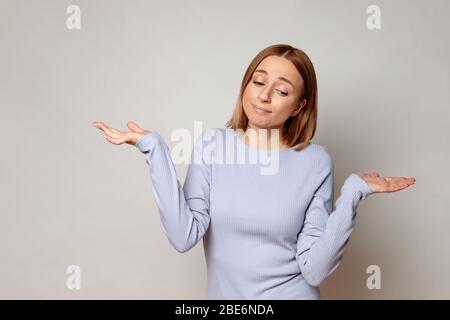 I don't know! Close up studio portrait of shy awkward young woman feeling embarrassed, confused and puzzled, shrugs shoulders, does not know what happ Stock Photo