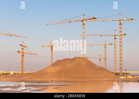 High pile of sand and group high-altitude tower cranes at construction site, sunset sky background.Future residential complex. Stock Photo