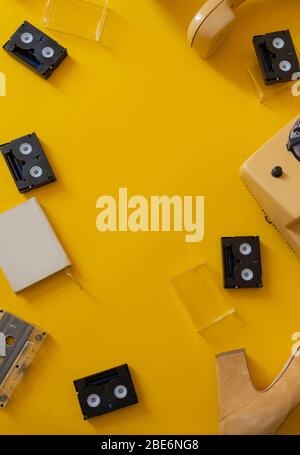 Retro black video cassettes tape and old vintage yellow phone on the yellow background, top view, copy space. Stock Photo