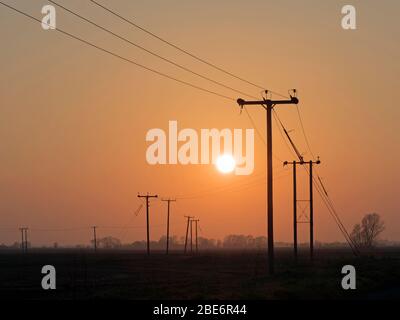Sun setting in fenland, with telegraph poles in the foreground, near Aldreth, Cambridgeshire, England Stock Photo