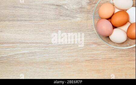 background - a glass bowl with multi-colored eggs stands on a wooden surface, top view, Stock Photo