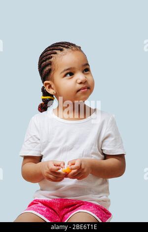 Little girl eating a tangerine while looking up at her parent over blue Stock Photo