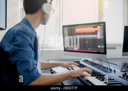 composer hands on piano keys in recording studio. music production technology, man is working on pianino and computer keyboard on desk. Stock Photo