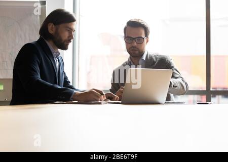Male coworkers sit at meeting working on laptop together Stock Photo