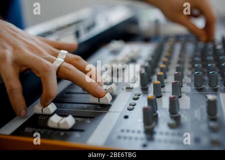 Hand on a mixer, operating the leader. Sound engineer working at mixing panel in the recording studio. Hands adjusting audio mixer. Close up concept. Stock Photo