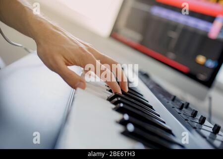 composer hands on piano keys in recording studio. music production technology, man is working on pianino and computer keyboard on desk. close up Stock Photo