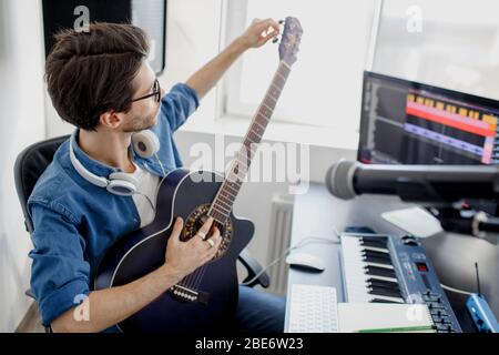Man plays guitar and produce electronic soundtrack or track in project at home. Male music arranger composing song on midi piano and audio equipment Stock Photo